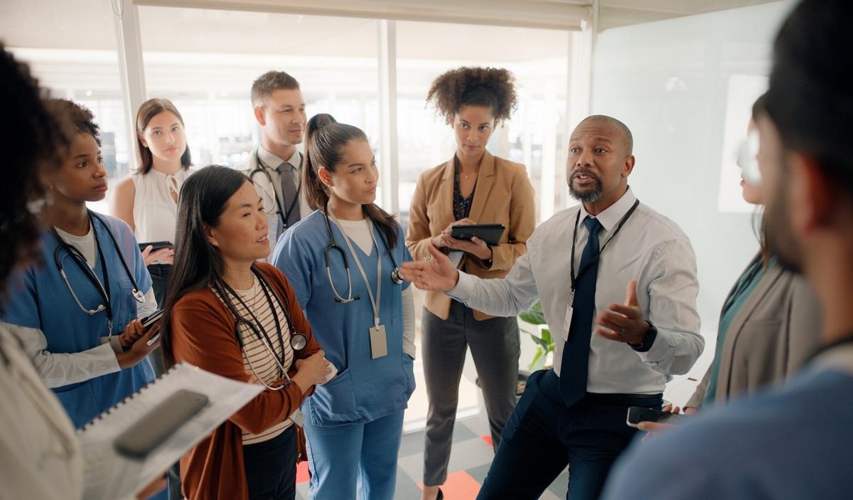 Boardroom, discussion and executive talking to staff in hospital for healthcare of patients. Man, training and mentor of employees or nurses and tablets for notes of speech by leader in medical field